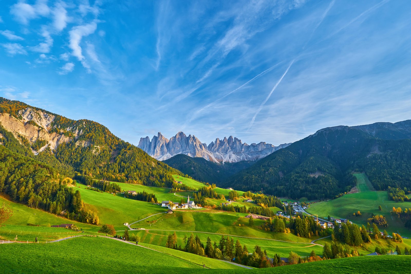 Amazing autumn scenery in Santa Maddalena village with church, colorful trees and meadows under rising sun rays. Dolomite Alps, Italy.